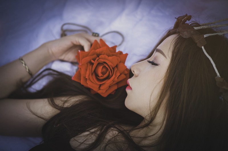 Man sieht eine Frau ohne Schlafanzug neben einer Rose schlafen.