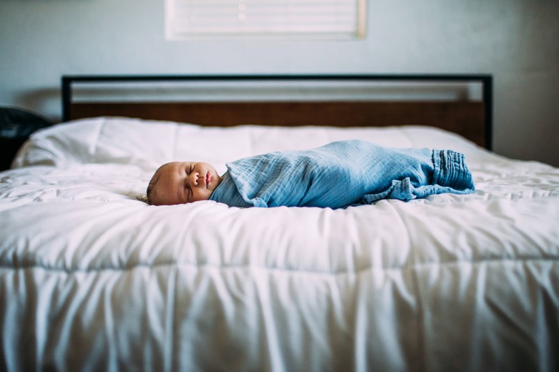 Man sieht ein kleines Neugeborenes, das auf dem Bett schläft