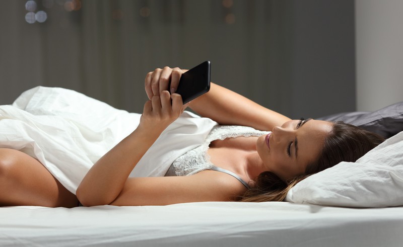 Frau liegt im Bett mit Handy