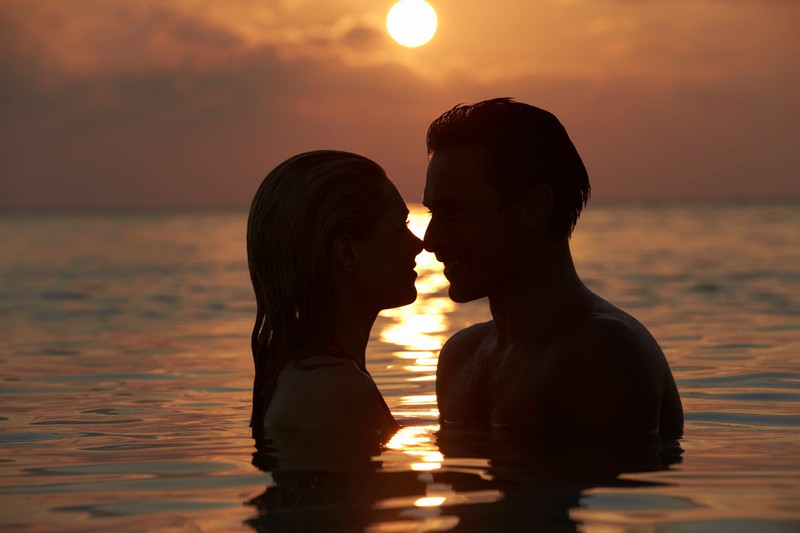 Eine Frau und ein Mann, die sich romantisch beim Sonnenuntergang küssen wollen. Seine Körpersprache signalisiert es
