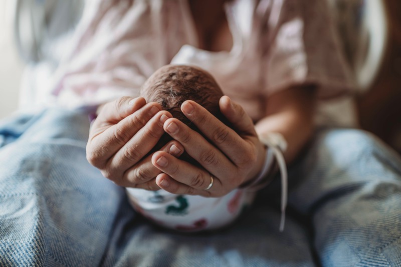 Ein Bild einer frischgebackenen Mama, die ihr neugeborenes Baby im Arm und in den Händen hält