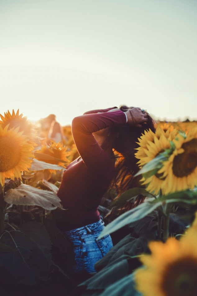 Frau, die im Spätsommer auf einem Feld voller Sonnenblumen steht