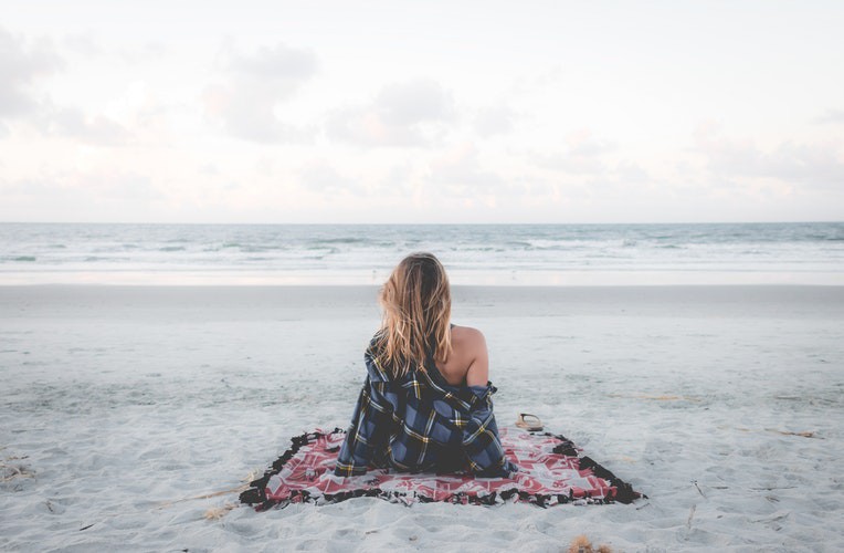 Eine Frau sitzt am Strand und es geht um die After Sun Pflege nach einem Sonnenbad.