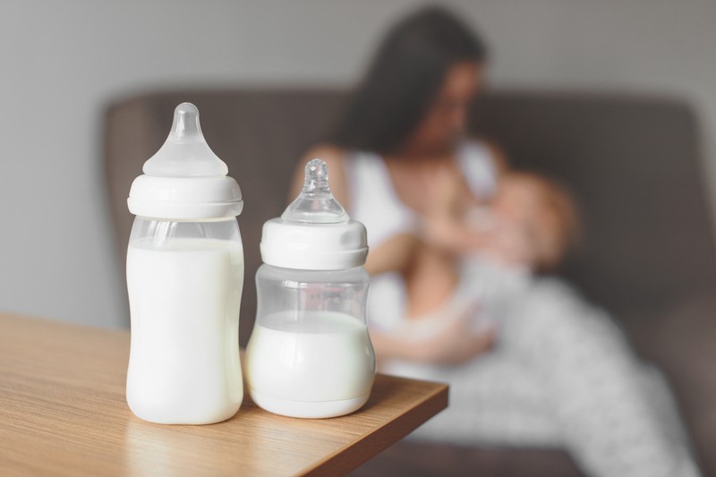 Mutter füttert ihr Kind, im Vordergrund zwei Milchflaschen