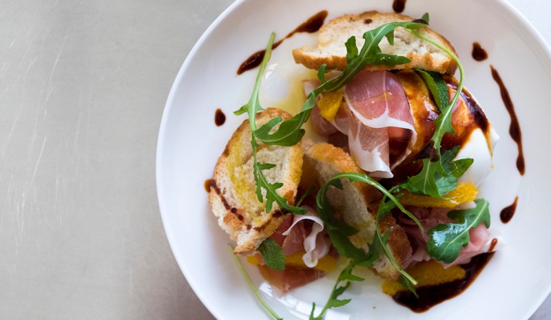 Man sieht Bresaola-Röllchen, die mit Pistazien und Rucola verziert werden