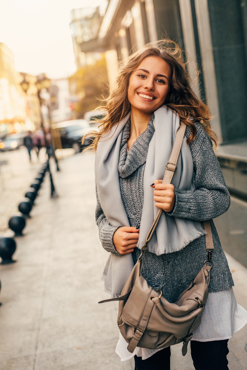 Frau mit langen, lockigen Haaren und Wollpullover strahlt