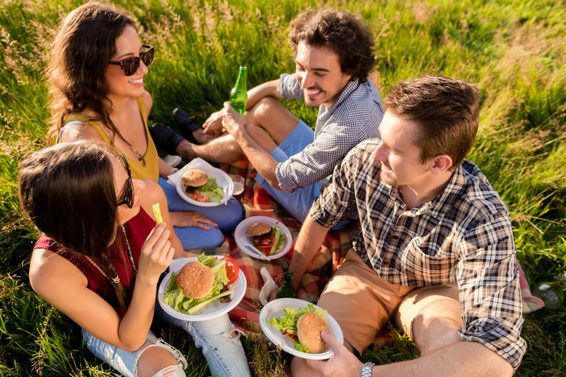 Freunde sitzen gemeinsam im Gras und essen Burger