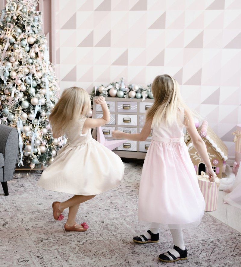 Zwei süße Mädchen, die mit ihren Kleidern am Weihnachtsbaum tanzen