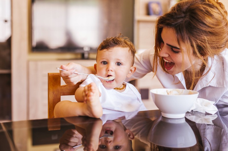 Eine Mutter kann ihrenmBaby Brei selber machen und füttert es mit einem Milch-Getreide-Brei
