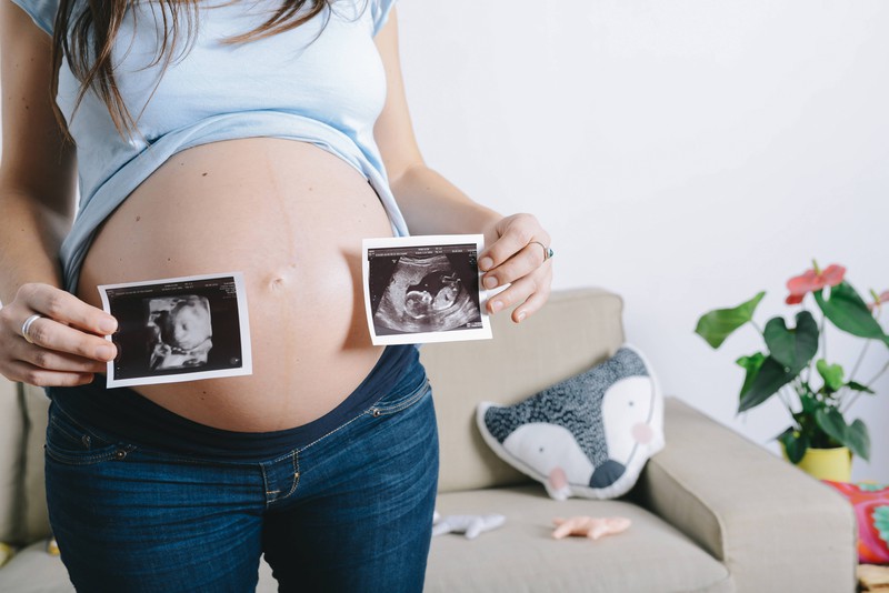 Schwangere Frau zeigt die Ultraschallbilder ihrer letzten Untersuchung.