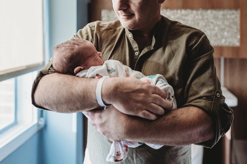 Ein Vater, der sein eigenes Kind kurz nach der Geburt auf dem Arm hält
