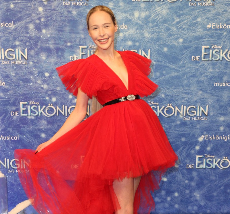 Theresia Fischer in einem schönen roten Kleid mit Spitzenschuhen, mit sehr dezentem Make-up.