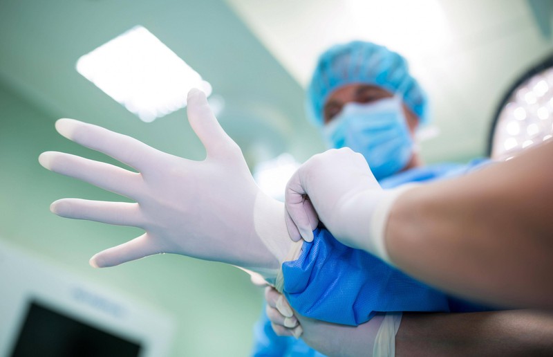 Frauenarzt oder -ärztin zieht sich die weißen Einweghandschuhe an für eine Untersuchung.
